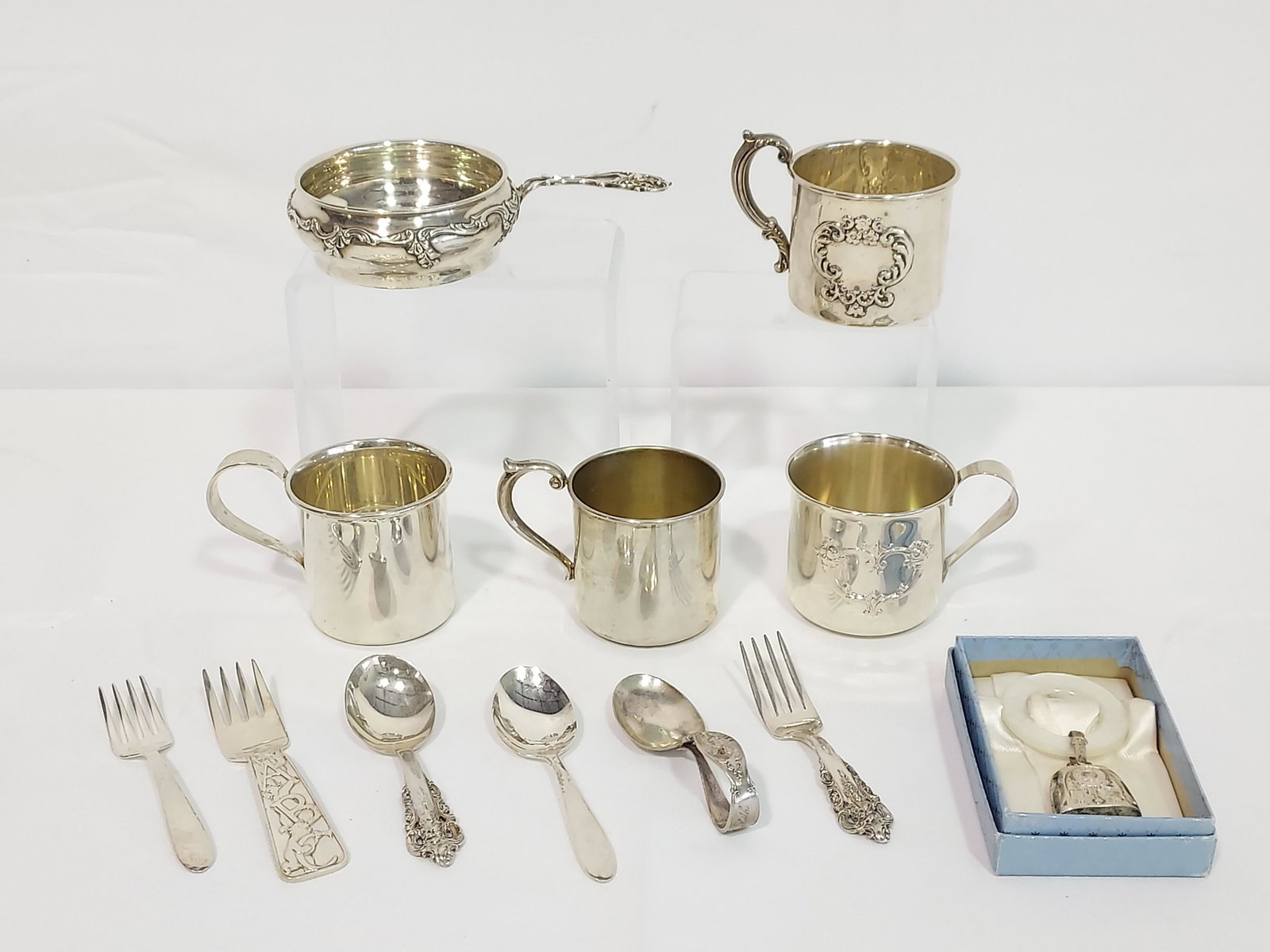 CHILD & BABY STERLING SILVER KEEPSAKES CUPS FLATWA: A collection of children and baby sterling silver keepsakes including: A Tiffany & Co ABC fork, Wallace Grand Baroque spoon and fork, Lunt spoon and fork, an unbranded sterling silver, folded handle b