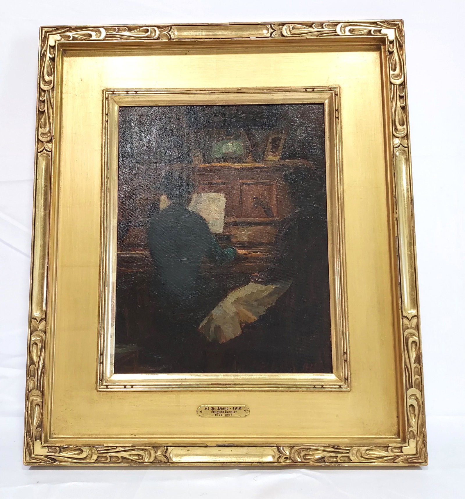 AUGUSTE KOHLER OIL ON BOARD PAINTING: AT THE PIANO: Auguste Kohler oil on board painting, titled on plaque "At the Piano", dated 1919. Framed measuring a total of 21.75" tall x 18.5" wide. Sight area measures 13.5" x 10.5". Signed and dated lower right