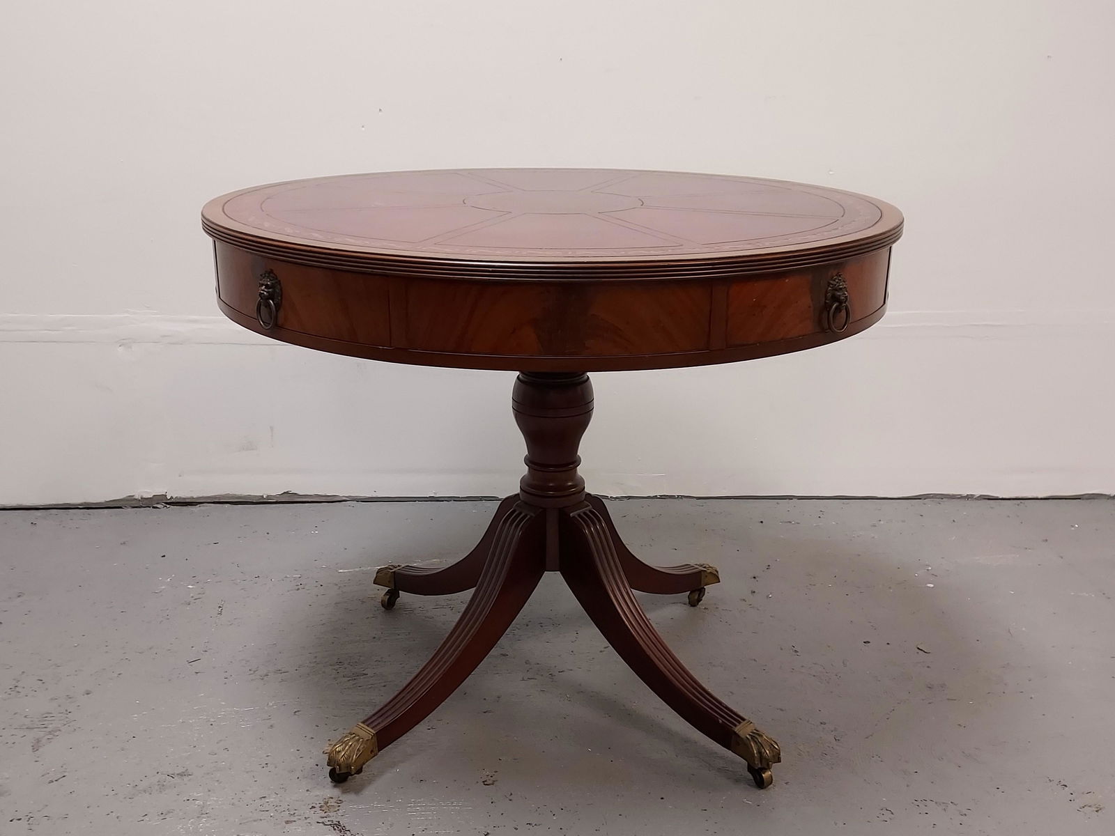 BEACON HILL DUNCAN PHYFE STYLE LEATHER TOP TABLE: Vintage Beacon Hill Collection Duncan Phyfe style embossed leather top pedestal center table measuring 29" tall x 36" diameter. Tag inside drawer. Flame mahogany finish with brass claw feet on castors