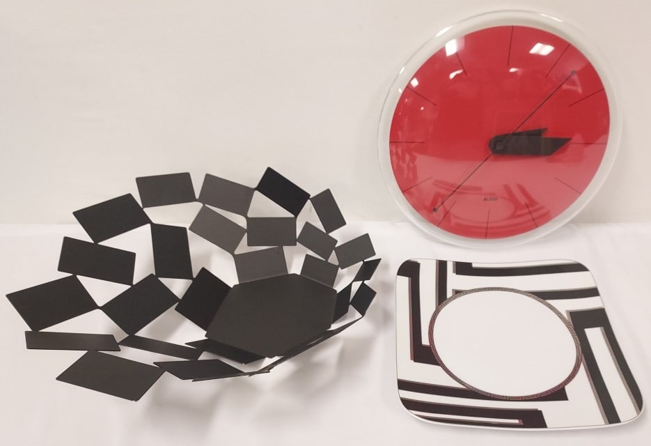 3 pcs - ALESSI CENTERPIECE AND CLOCK, VERSACE PLA: Three piece lot . A Versace Dedalo 10.5" plate. Ai La Stanza Dello Scirocco Centerpiece designed by Mario Trimarchi for Alessi in stainless steel with a black epoxy covering., which measures: 6" tall