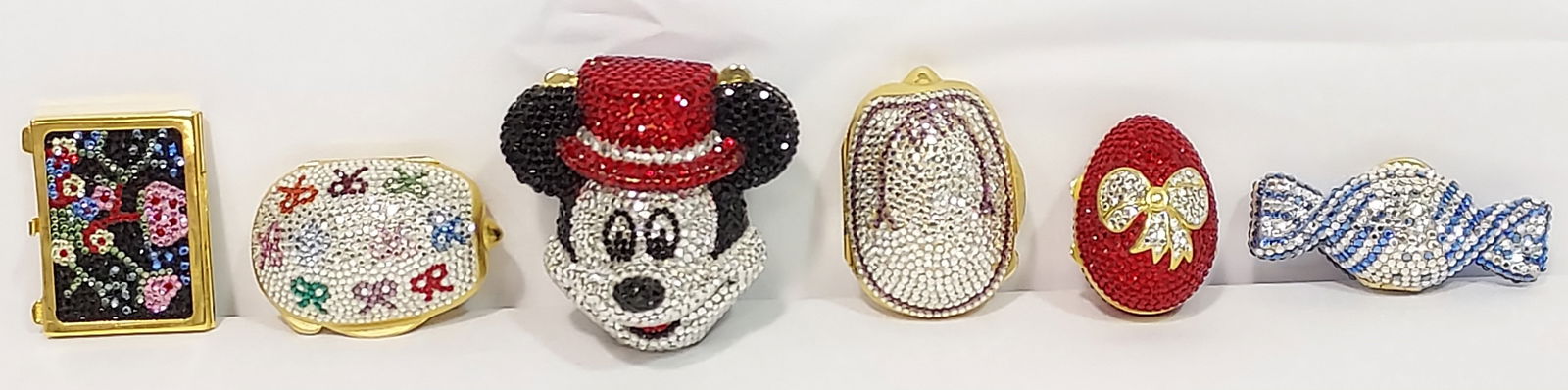 FIVE JUDITH LEIBER SWAROVSKI CRYSTAL PILL BOXES +: Lot of five Judith Leiber Swarovski crystal clad pill boxes, plus one unbranded Mickey Mouse form box. Longest Judith Leiber is the candy form box at 2.6" long. All are signed at rim except the unbran