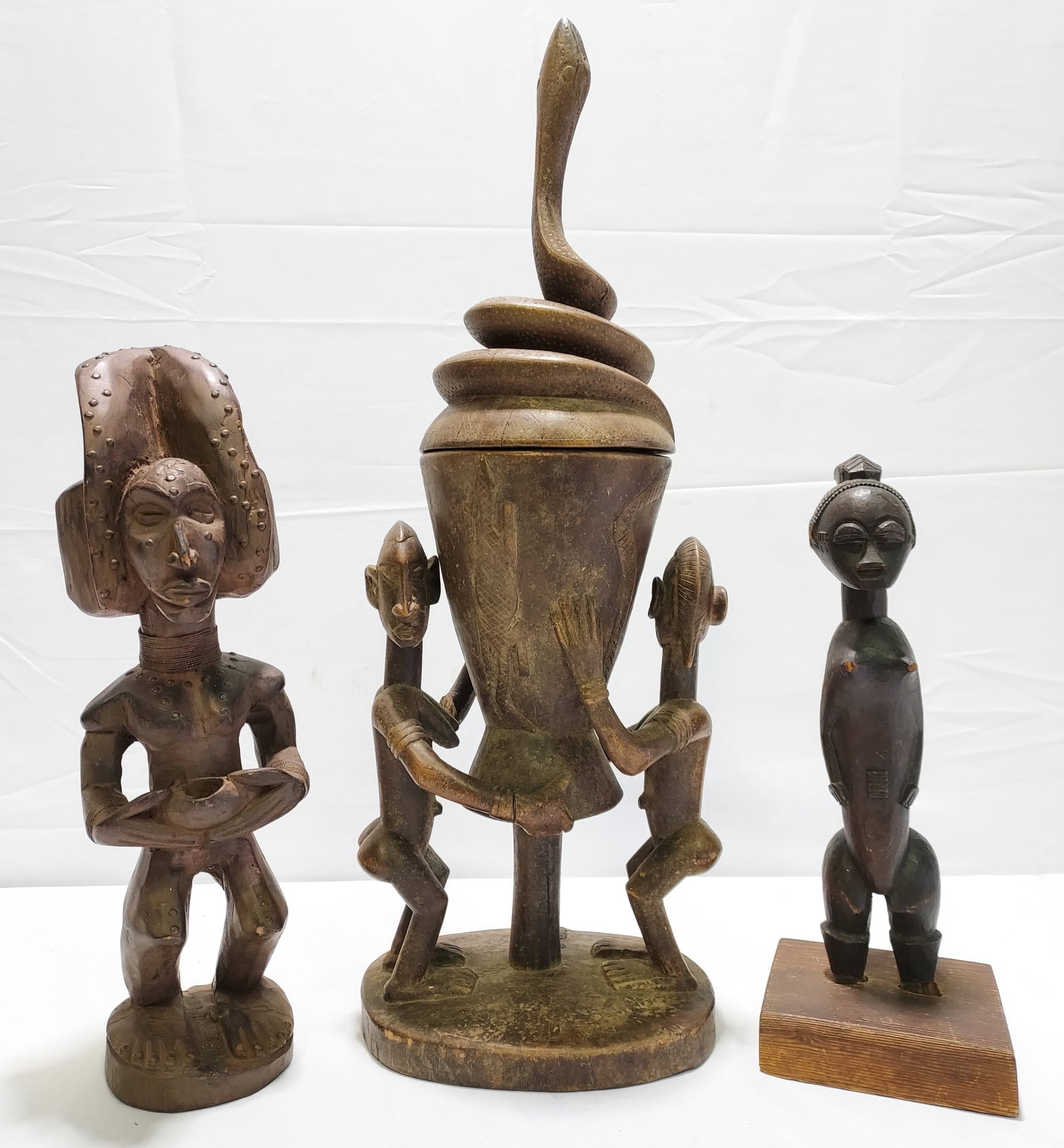 AFRICAN CARVED WOOD FIGURES AND CEREMONIAL URN: Three African carved wood items. 1) A carved wood effigy of a nude female figure, dark stain, raised scarification to face, stomach, upper and lower back, peg type carved lower leg/fee to fit square w