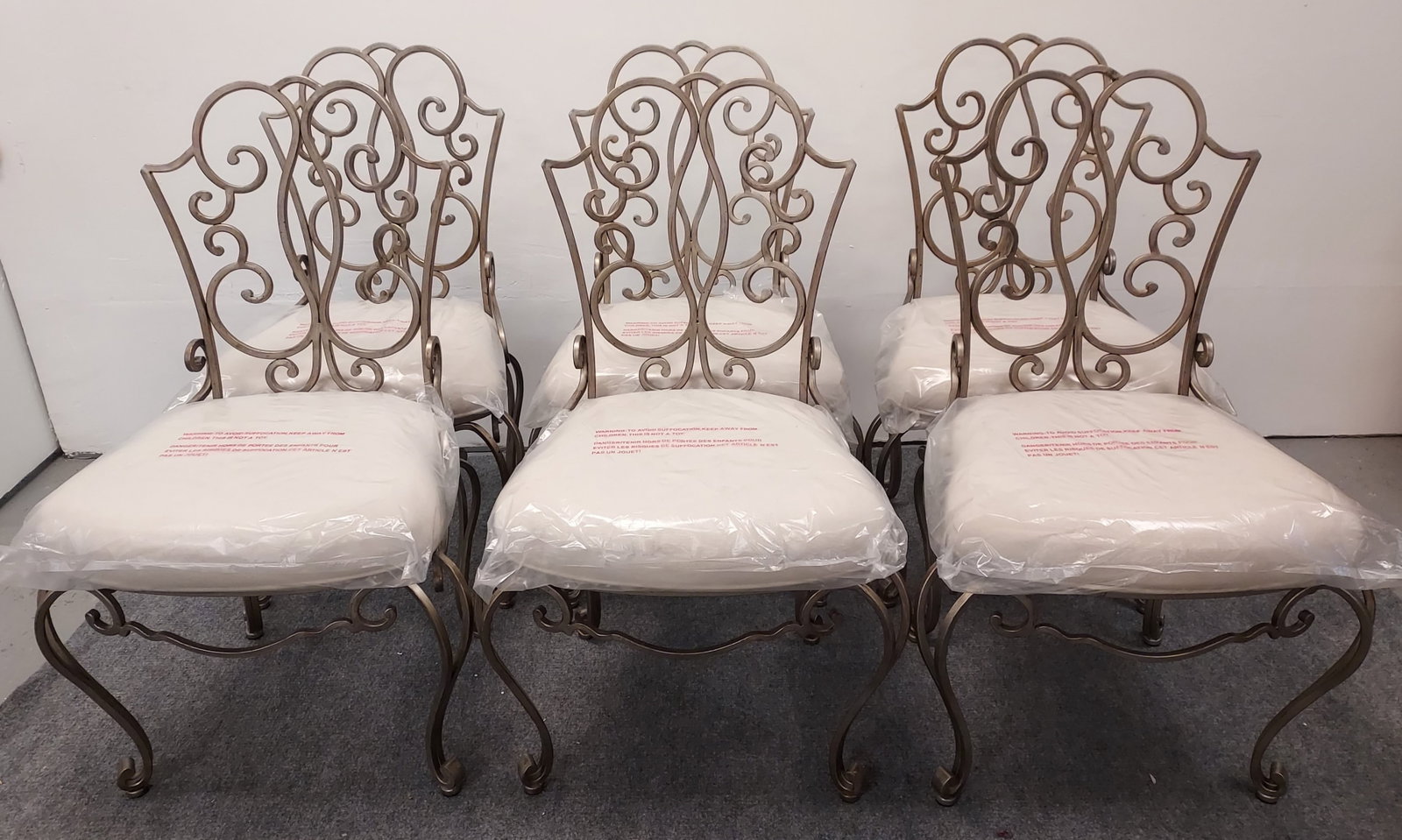 SIX MODERN BOMBAY SCROLLED IRON DINING CHAIRS: Lot of six modern Bombay scrolled iron dining chairs, each measuring 38" tall X 19" wide and 23" deep. New off-white fabric upholstery still covered with original plastic protectors. Condition: good, 