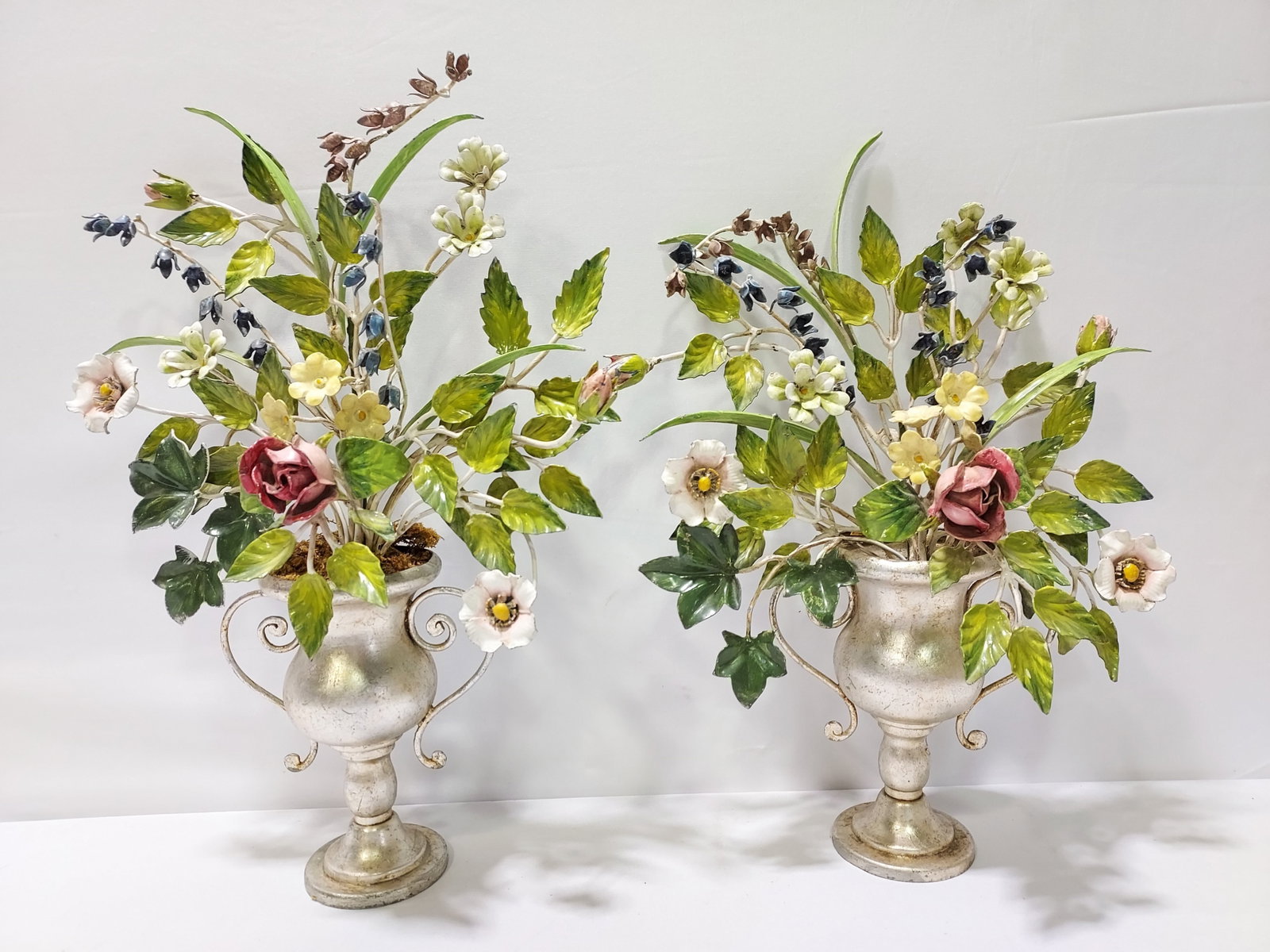 TWO VINTAGE ITALIAN TOLEWARE FLORAL ARRANGEMENTS: Lot of two vintage toleware floral arrangements. Both in small platinum finish footed pots / urns. One has floral to hold the arrangement in place, and the other is just propped up in the urn. The one