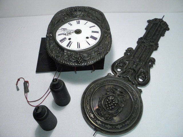 GERMAN MORBIER WAG ON WALL CLOCK: German Morbier (Wag on Wall) clock. Box design with grape vine and wheat pattern embossed metal and pendulum, brass works. White enamel face with standard Roman numeral numbering on dials. Includes we
