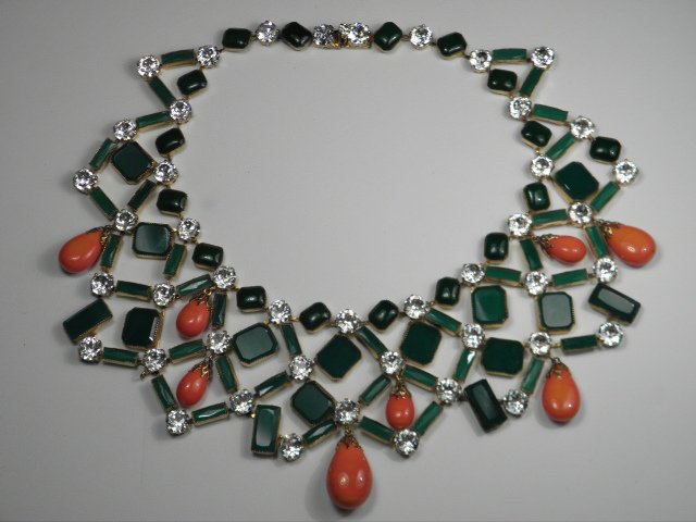 KENNETH JAY LANE GREEN & ORANGE BIB NECKLACE: Kenneth Jay Lane bib necklace with green faceted glass, rhinestones, and swirled orange glass tear drops throughout. Green glass cabochons decorate the inner edge around the neck. All set in a gold to
