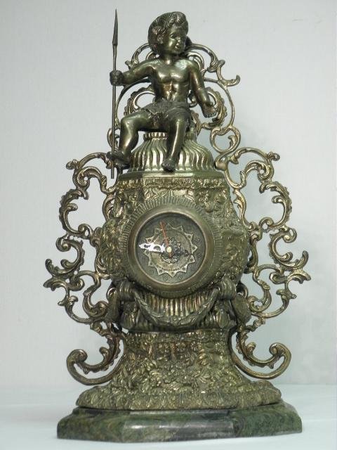 FRENCH ORMOLU BRASS FIGURAL MANTLE CLOCK: French ormolu brass figural mantle clock. Pierced brass fretwork decoration on each side, with a carved green marble base and figural cherub sculpture at the top. Brass clock face with a replaced batt