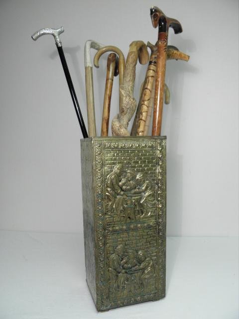 SQUARE BRASS UMBRELLA STAND WITH 10 ASSORTED CANES: Square brass umbrella stand with ten assorted canes. The umbrella stand is wooden with a repousse brass overlay, and a tin slide out tray at the bottom. Canes include wood, tusk, and silver toned meta