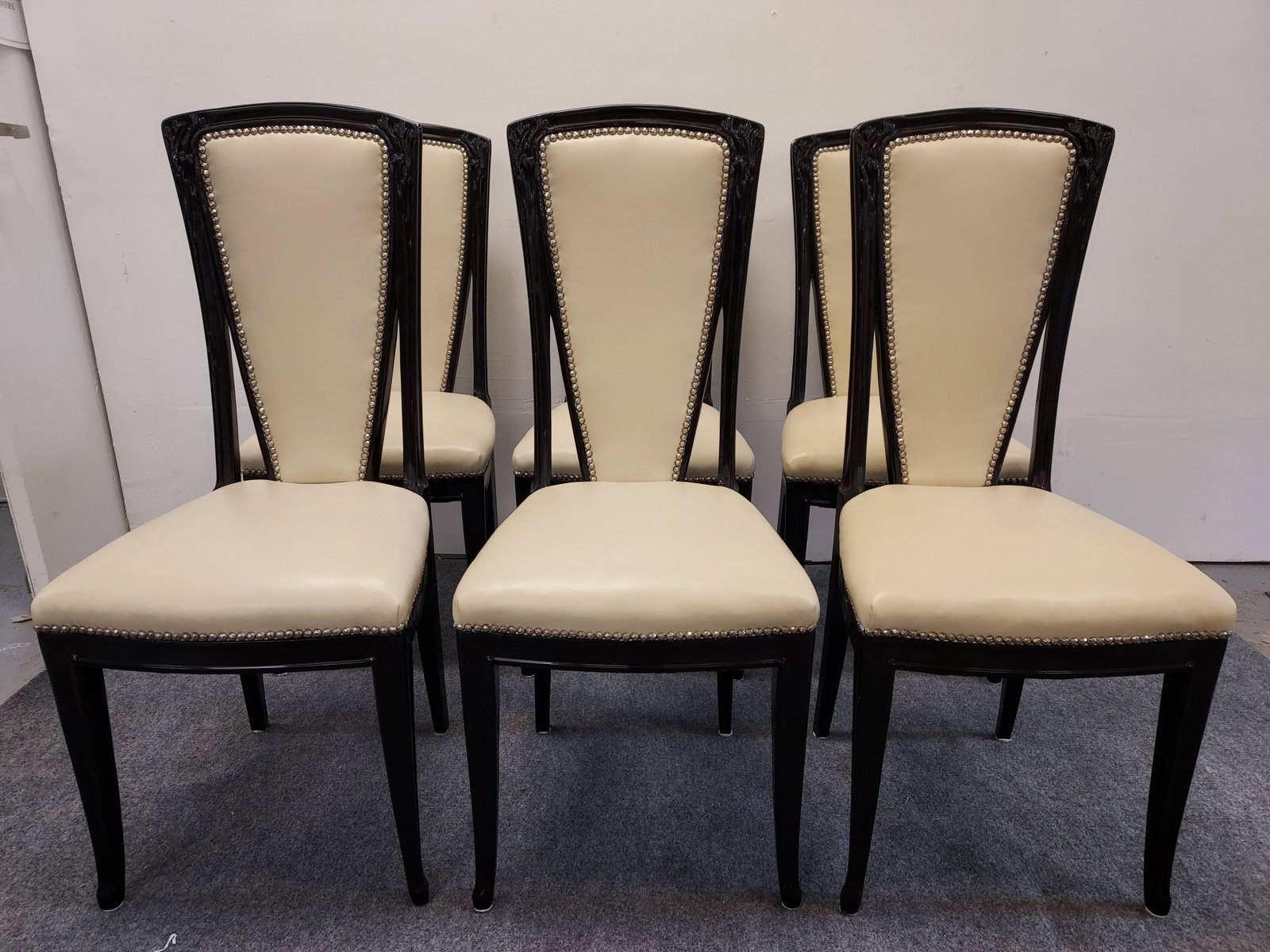 6 ART DECO INFLUENCE DINING ROOM CHAIRS: 6 Art Deco influence dining room chairs; black lacquer carved wood with ivory leather upholstery and silver tone hammered nail heads. Wood is relief carved with a floral design. Condition: chairs show