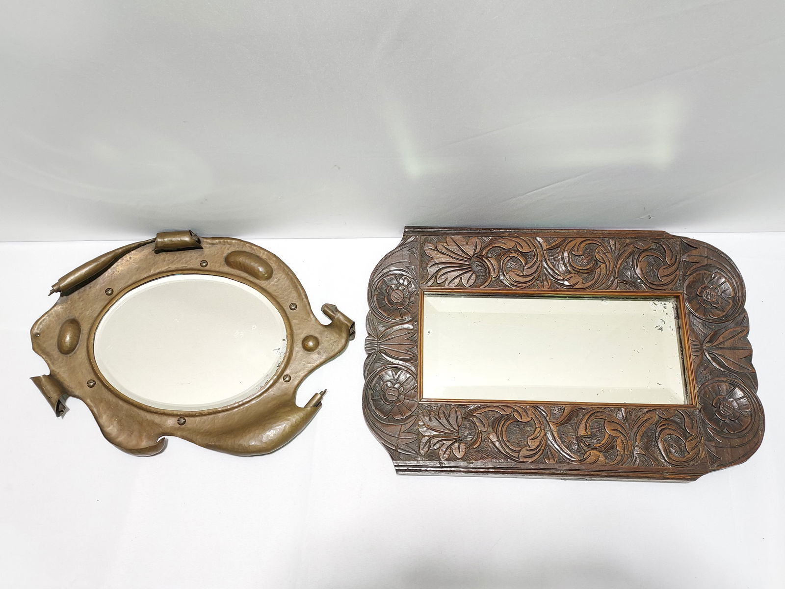 2 ARTS & CRAFTS MIRRORS 1 COPPER 1 CARVED WOOD: Two Arts & Crafts antique mirrors. The first a copper hand-hammered oval mirror with curled sides, beveled oval mirror, and screw & bolt design with functionality. Back plate is held on with the screw