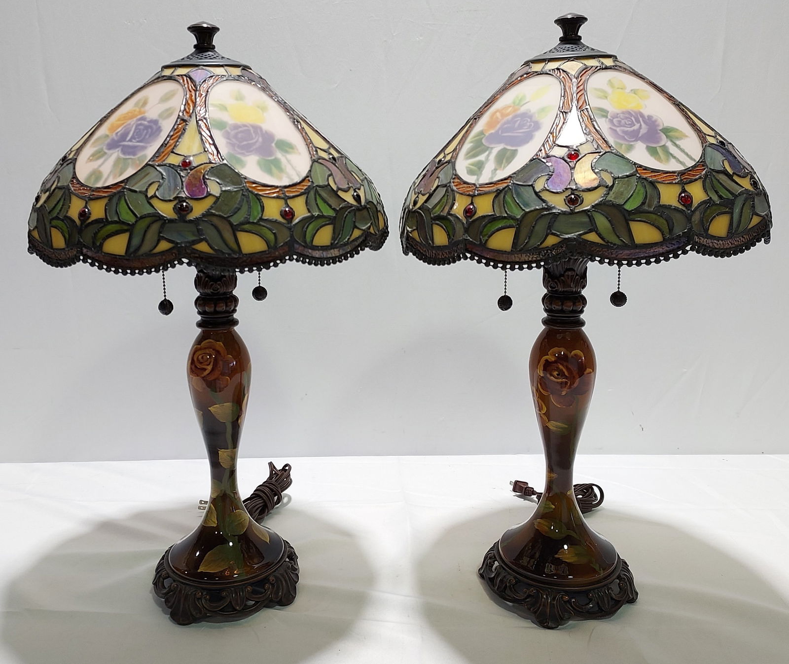 PAIR DALE TIFFANY STAINED LEADED GLASS TABLE LAMPS: Pair of Dale Tiffany Antiques Roadshow series stained and leaded glass table lamps, each measuring 27" tall x 16" diameter at the shade. Reverse painted glass main body, with patinated bronze style ba