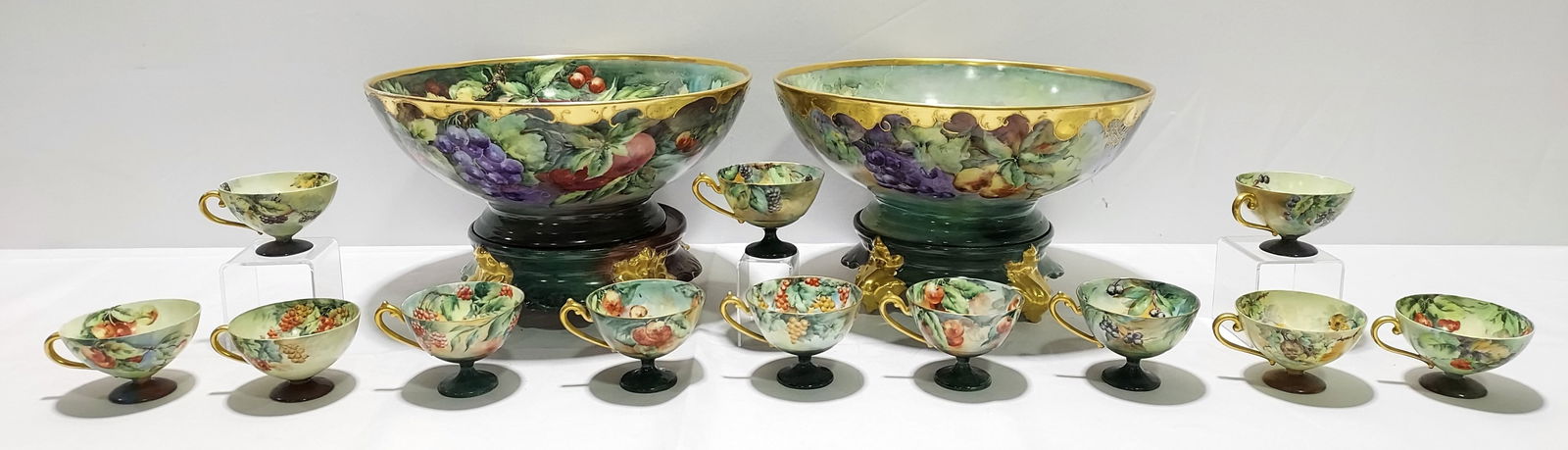 TWO LIMOGES HAND PAINTED PORCELAIN PUNCH BOWLS W C: Two Limoges hand painted porcelain footed punch bowls with cups. Includes one 14" diameter punch bowl and one 13.75" diameter punch bowl, both with separate stands, (6) 2.25" tall footed cups, and (6)