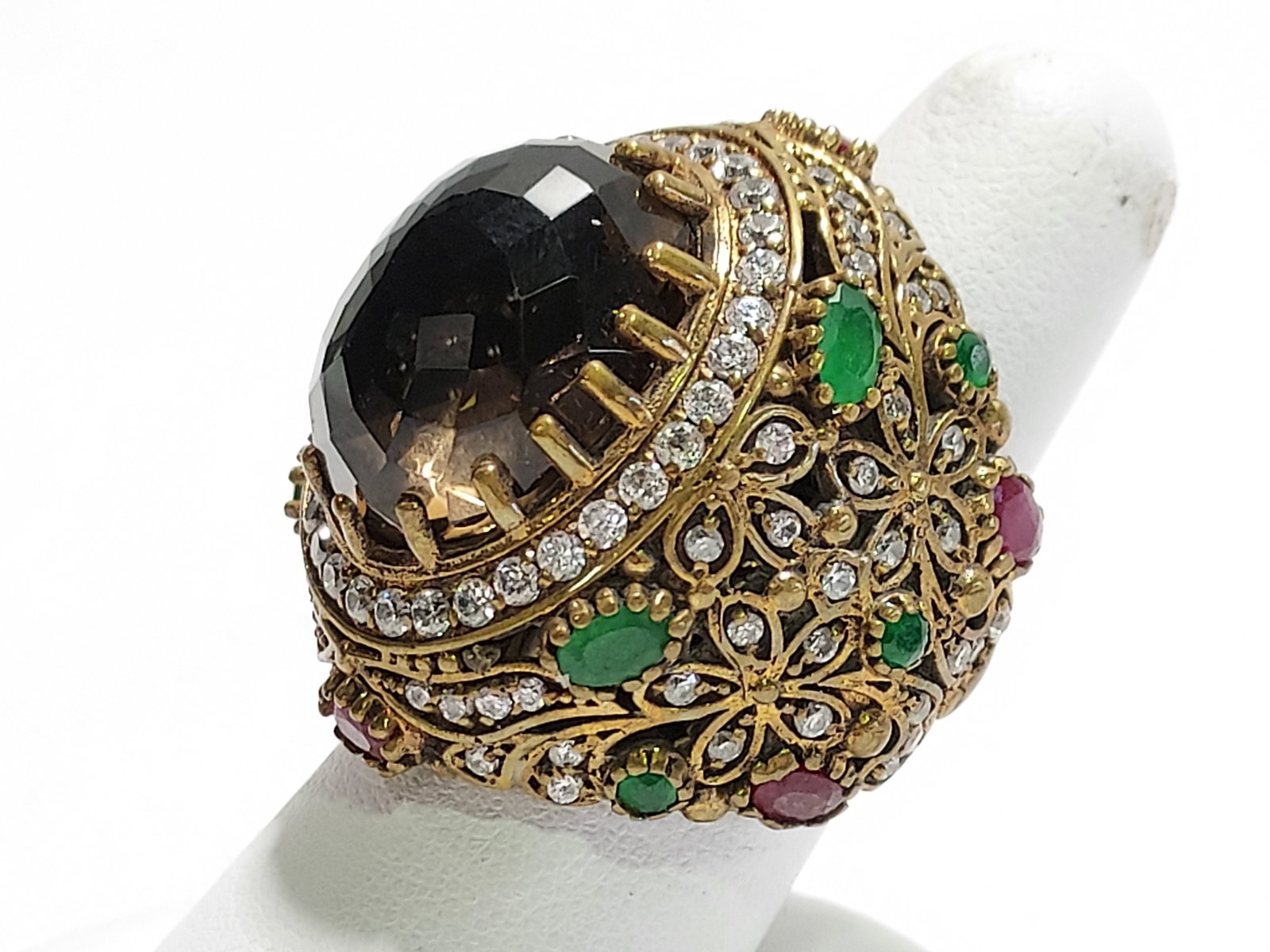HJ26 Smoky quartz ring with emeralds & rubies: Smoky quartz ring with emeralds & rubies. Large oval shaped smoky quartz (16.5mm x 20mm) surrounded by whites stones, 2 oval emeralds, 3 round emeralds, and 4 oval shaped rubies. Brass over silver. 18