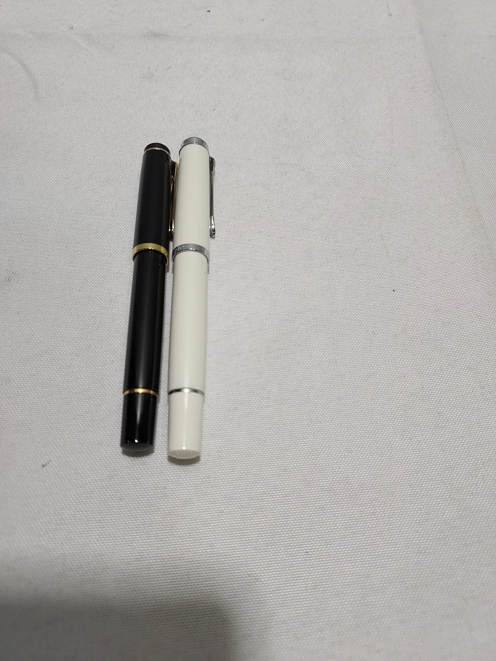 H368 2 Pelikan fountain pens: 2 Pelikan fountain pens: 1 black with gold tone metal trim, 1 white with silver tone metal trim, both with dried and crusted ink in and around the nib.
