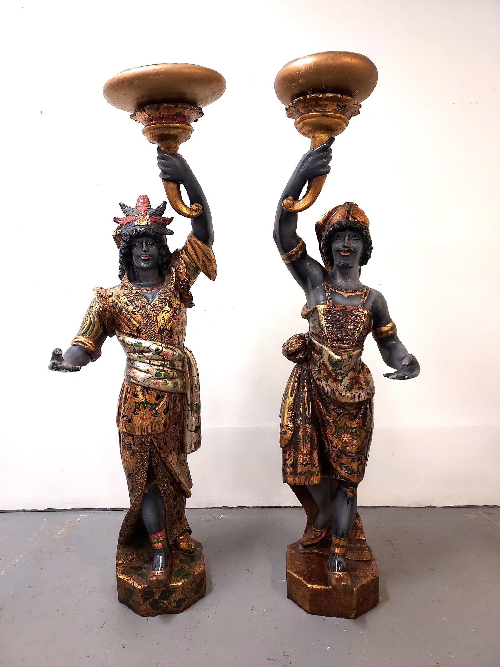 H1 Pr Lifesize Fiberglass Blackamoors Figures: A pair of Venetian style fiberglass Blackamoor figures; each with parcel gilt, polychrome decorated, having a gilded torch with later applied bowls to torches. Both with octagonal pedestals. Age crack