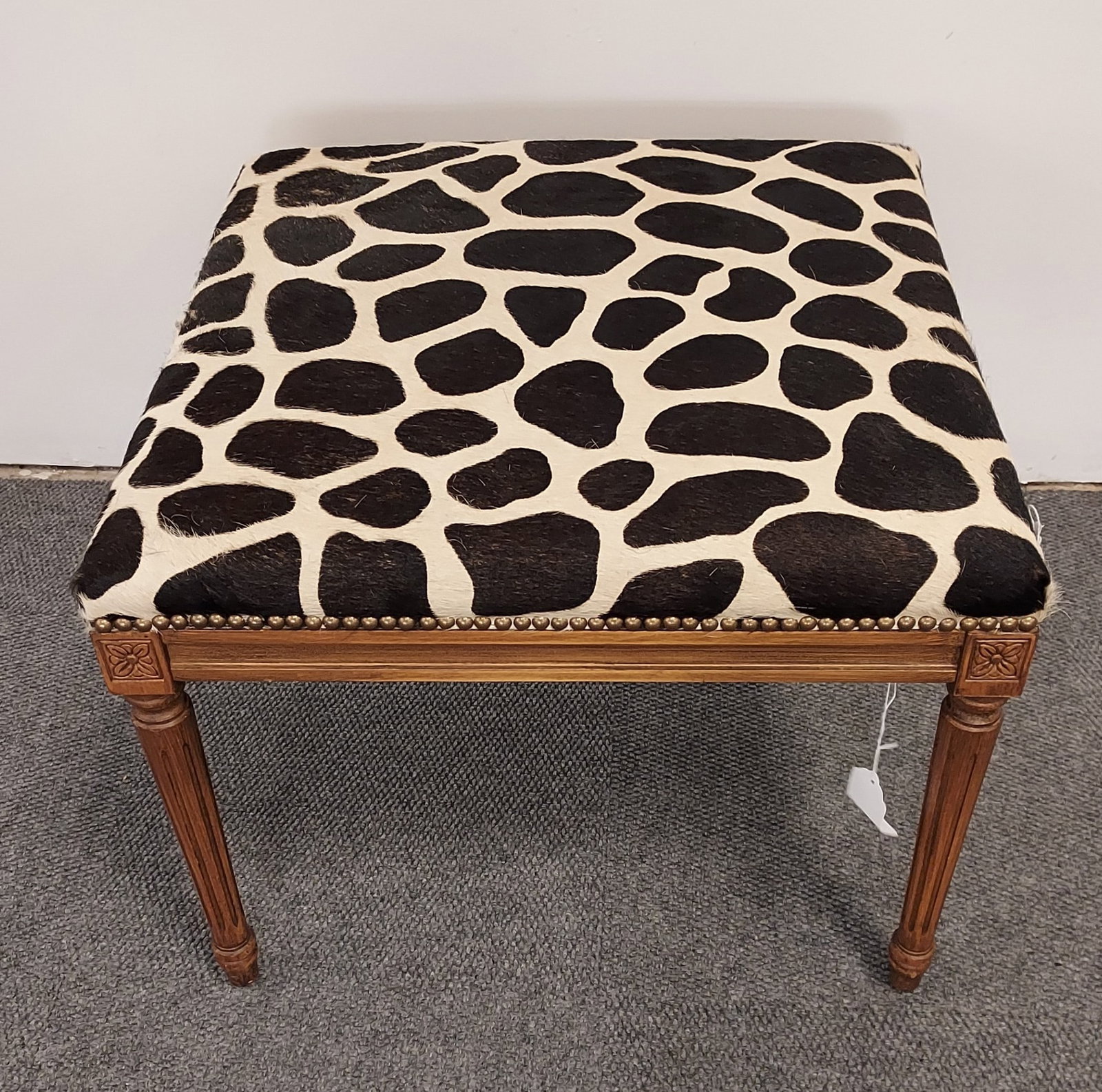 H1578 Ottoman with dyed animal spot cowhide uphols: Ottoman with dyed animal spot cowhide upholstery and nail heads: Unbranded, French-style fluted and tapered legs with carved rosettes on the corners of the apron. 18.5" x 23.75 x 23.75. 3rd quarter 20