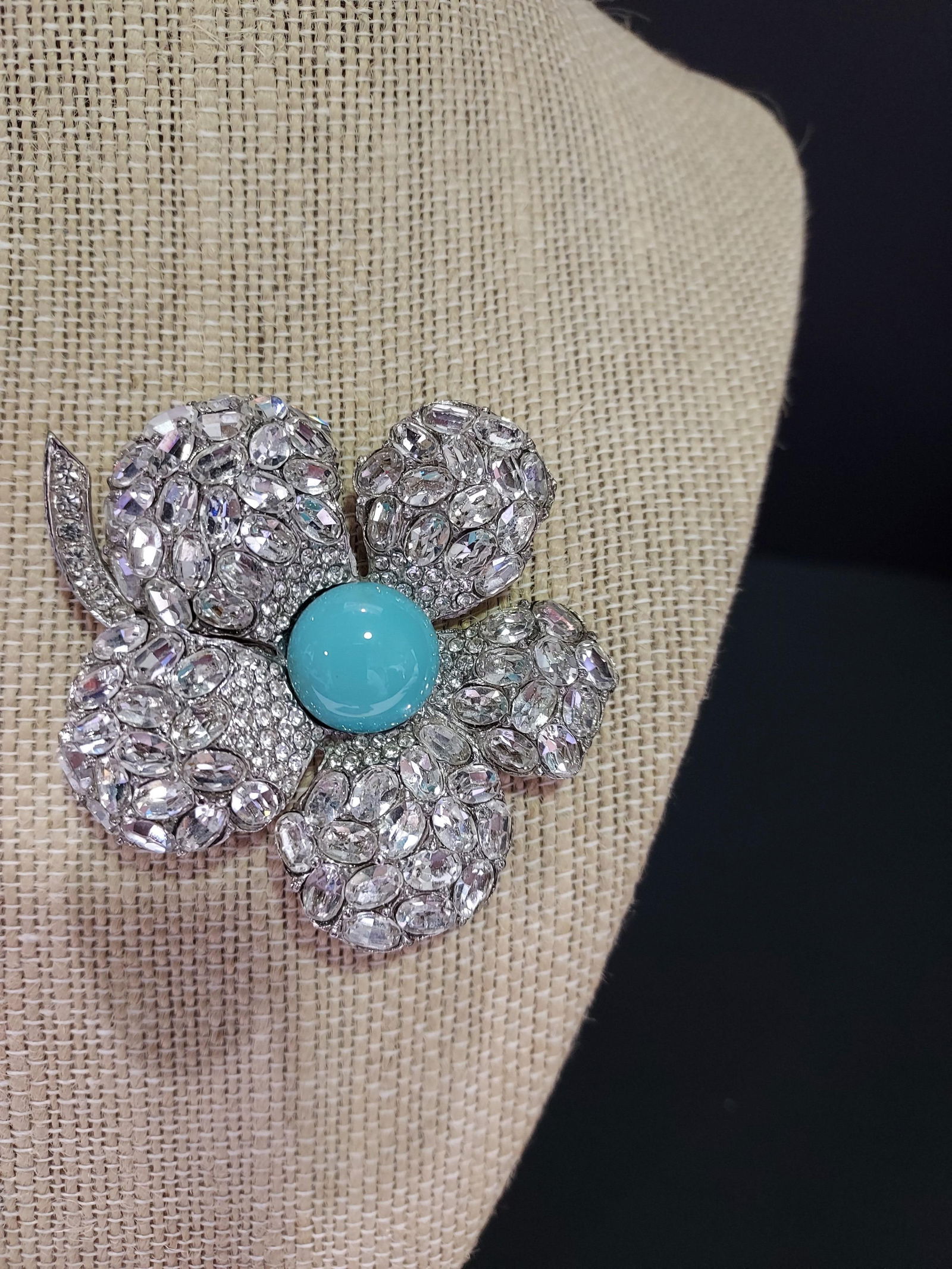 H592 Ciner floral brooch: Ciner floral brooch: 5 petal flower on white metal with large oval clear rhinestones and small round clear rhinestones close to center. Center stone is a robin's egg blue half bead. 2.5"