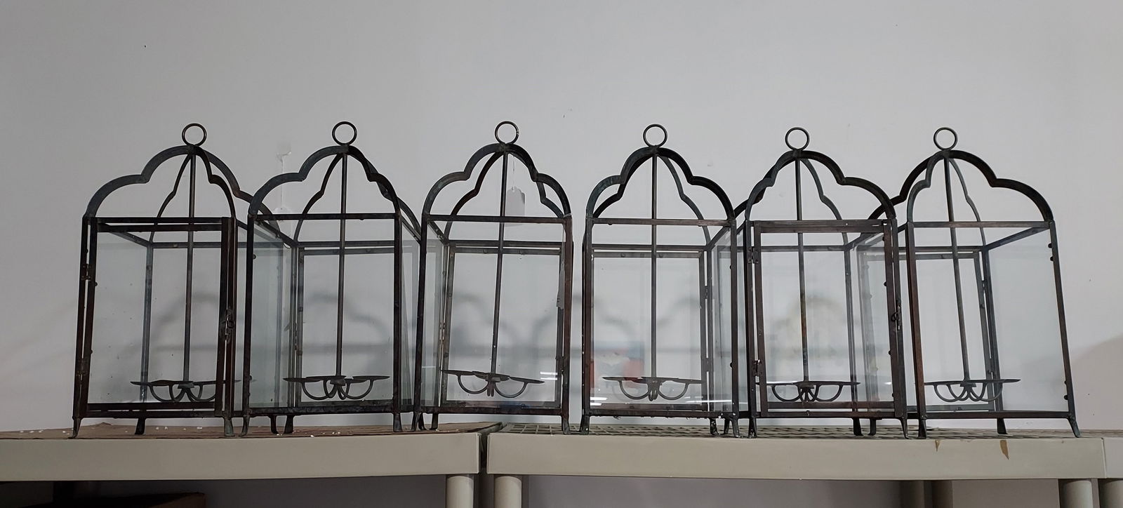 H1524 Ten bronze and glass pillar candle lanterns: Ten bronze and glass pillar candle lanterns: each with a circular Ten bronze and glass pillar candle lanterns for hanging and a welded rod ending in four round plateaus for the candles. 21" x 9" x 8".