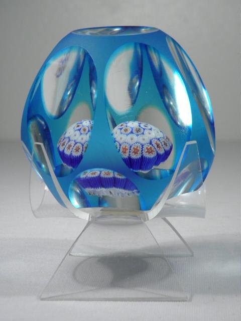 BLUE CUT TO CLEAR GLASS MILLEFIORI PAPERWEIGHT: Blue cut to clear glass millefiori paperweight. Faceted sides with a red, white, and blue millefiori medallion in the center. Unsigned, thought to possibly be Whitefriars. Condition: very minor imperf