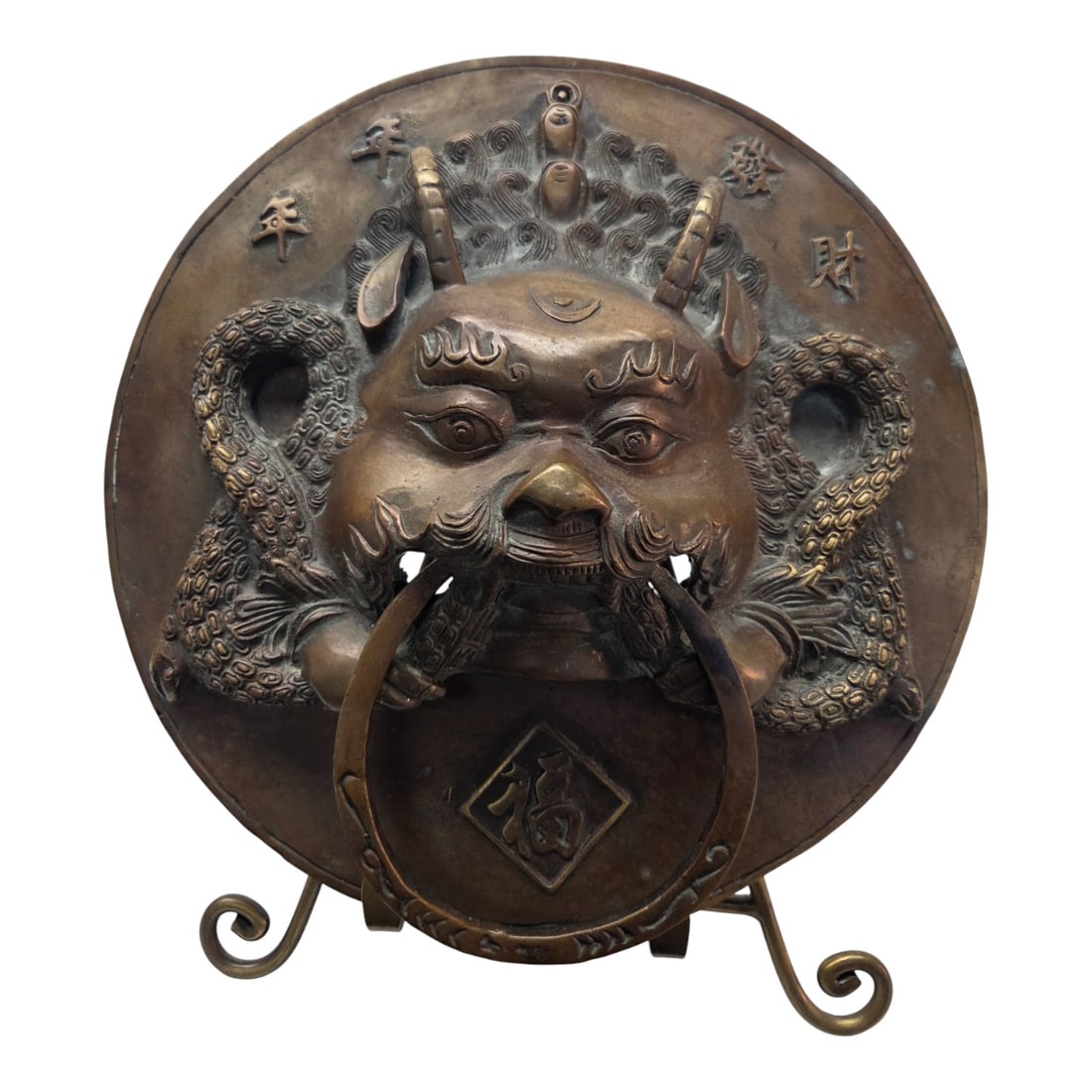 ASIAN STYLE BRASS/ BRONZE FOO DOG DOOR KNOCKER: Circular Asian style brass/bronze foo dog (head) door knocker with stand. No stamps on back. Measures 12"H x 11"W. Good condition. SHIPPING NOTE: Live Auctioneers offers a very convenient shipping