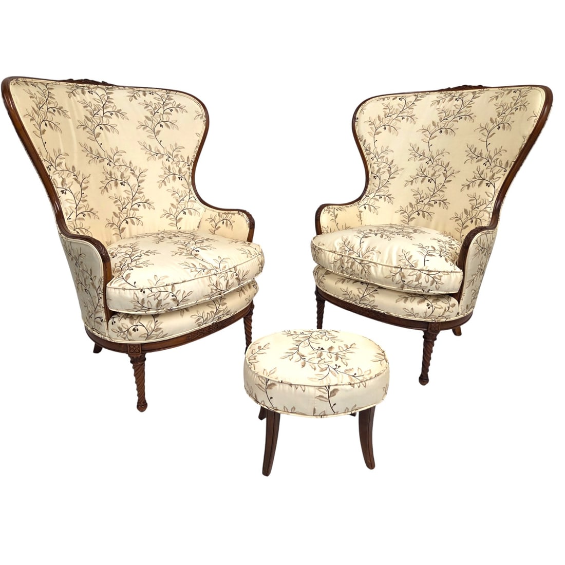 2 WINGBACK UPHOLSTERD CHAIRS W/ FOOT STOOL: Two carved wood upholstered (cream and brown floral) wing back chairs with single foot stool. Chairs measure 45"H x 31.5"W x 35"D. Foot stool measures 13"H x 17"W. Good condition. Minor wear due to
