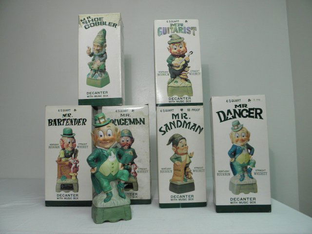 SIX HOFFMAN "LEPRECHAUN" CERAMIC MUSIC BOX DECANTERS: Lot of six vintage "Leprechaun" ceramic music box decanters by Hoffman Distilling Co. Condition: minor wear/signs of age to boxes or corks, see images. Largest boxes measure 14.3" tall x 7" x 6". Tota