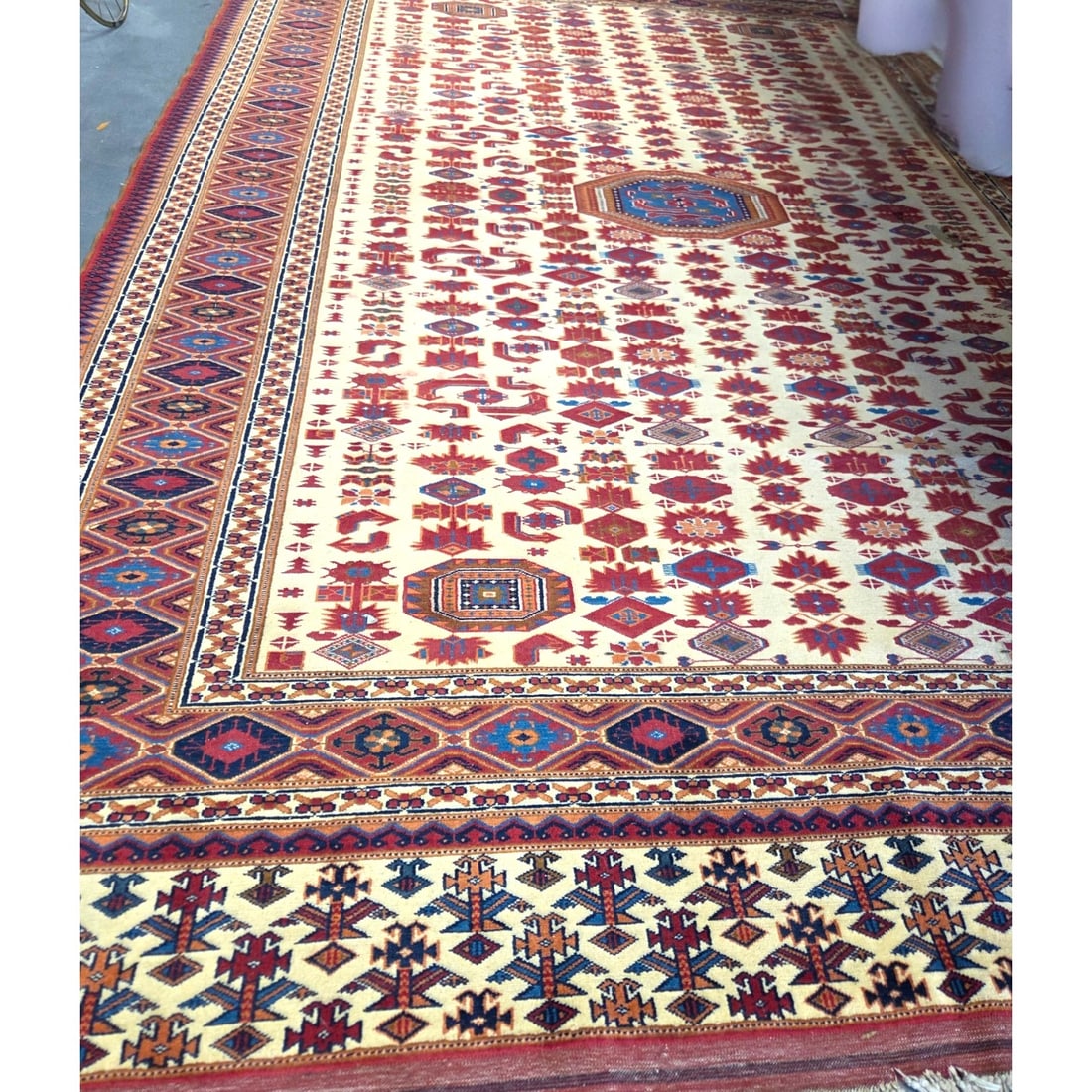 LARGE ORIENTAL RUG W/ GEOMETRIC DESIGN: Large Oriental wool rug featuring a cream background decorated with a repeating grid of geometric motifs, and stylized medallions. Includes a wide outer boarder filled with rich terracotta red and nav
