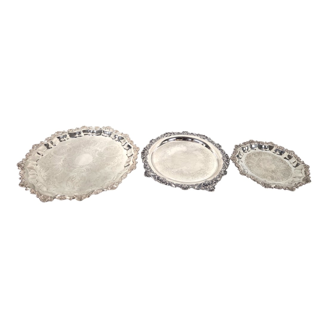 THREE ROUND DECORATIVE SILVER PLATED TRAYS: Lot of three footed round silver plated trays. These trays showcase heavy detailed scalloped boarders with intrigate scrollwork and floral motif. Elegant for dining or home decor. Largest tray