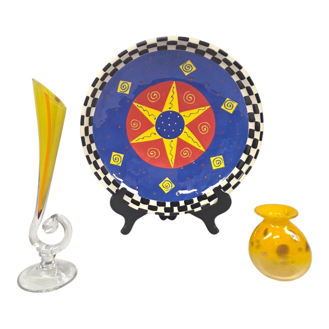 3 PC LOT OF SUNBURST CERAMIC PLATE & 2 STUDIO ART GLASS VASES: Three piece lot consisting of a whimsical hand painted ceramic serving bowl featuring a bold celestial yellow, blue, and orange sunburst motif and black and white checkered Mackensie-Childs style rim.