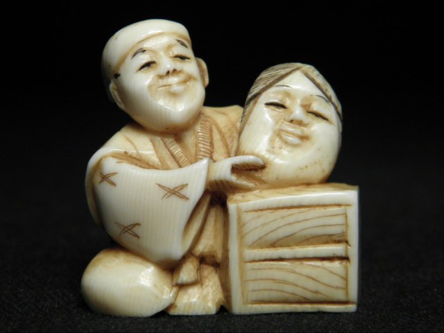 JAPANESE CARVED IVORY NETSUKE: MAN WITH MASK: Japanese carved ivory Katabori netsuke depicting a man with an Okame mask. Natural ivory color with black highlights, signed on base near loop holes. Condition: minor discoloration, see images. Measur