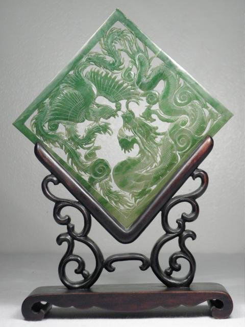 CHINESE CARVED GREEN JADE PLAQUE: A Chinese carved green jadeite square plaque. Carved and pierced with a dragon and phoenix pattern. Includes custom wooden stand. Condition: repair down the center of plaque, losses to intricate openw