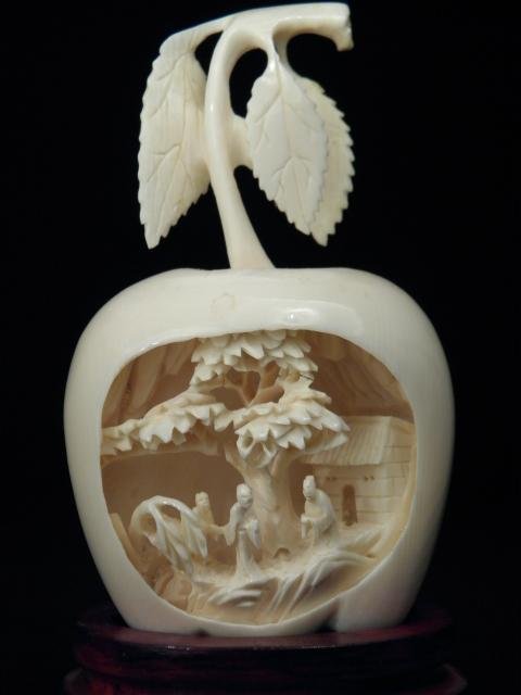 CHINESE CARVED IVORY APPLE DIORAMA: Chinese carved ivory apple form diorama. Diorama depicts an outdoor scene with three figures, a tree, and a house. Includes small carved wood fitted stand. Condition: very delicate age cracks to inter