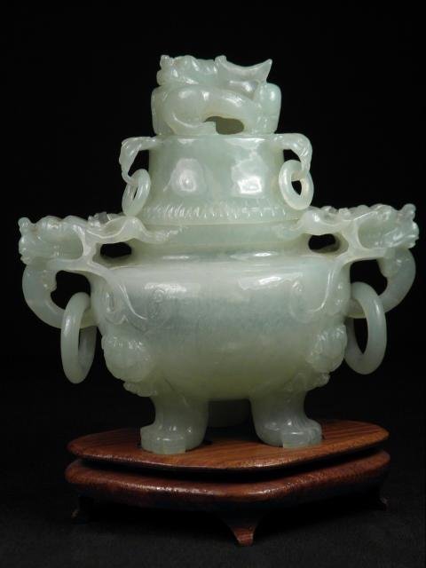 CHINESE CARVED GREEN HARDSTONE LIDDED URN: Chinese carved green hardstone lidded urn sitting upon three claw feet, with figural dragon handles and loops on each side. Lid is also adorned with a dragon form finial and three carved loop handles.