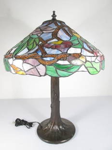 TIFFANY STYLE STAINED AND LEADED GLASS TABLE LAMP: Tiffany style stained and leaded glass table lamp. Tree trunk form base, with a slag, stained, and embossed glass shade in colors of green, orange, red, blue, etc. Condition: good, no cracked or