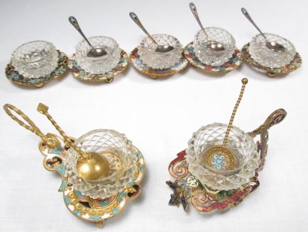 GROUP OF RUSSIAN ENAMELED SALT CELLARS W/RUSSIAN SILVER: Seven Russian enameled salt cellars holders with cut crystal cellar bowls. Included are (4) 875 silver spoons (2" long) with enameled handles and (2) brass enameled spoons. Condition: Wear commensurat