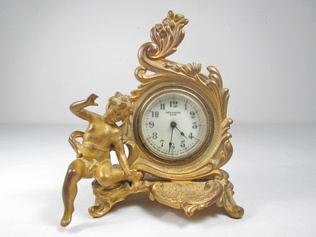 SMALL NEW HAVEN GILT METAL NOVELTY CLOCK: Small New Haven figural gilt metal novelty clock. Cherub to the left, with a shell form bowl below the clock face. Bevel glass crystal, marked on face by maker. Condition: wear to gilded finish, clock