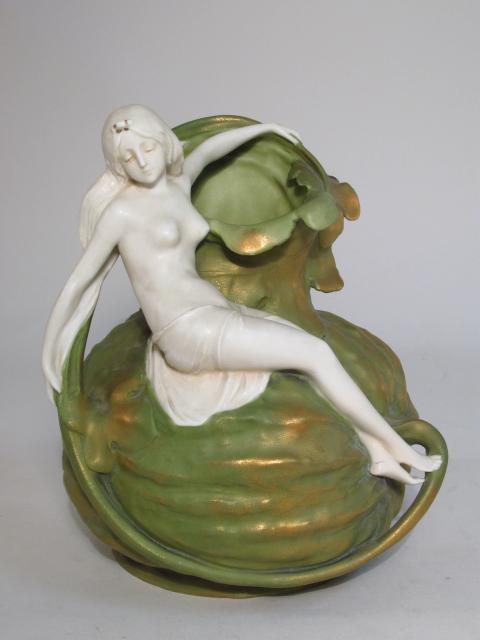TURN-TEPLITZ ART NOUVEAU POTTERY JUG BY ERNST WAHL: Turn-Teplitz Art Nouveau pottery jug by Ernst Wahliss. Depicts a maiden sitting on a gourd. Marked "Made in Austria 4754 6" on base. Condition: three small flakes to gourd leaf near rim, a few tiny im