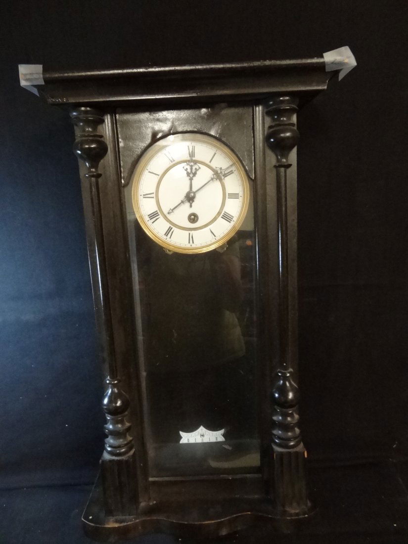 ''R = A'' DARK WOOD STAINED WALL CLOCK ENAMEL FACE WITH: ''R = A'' DARK WOOD STAINED WALL CLOCK ENAMEL FACE WITH BRASS RIM. THE CROWNS WOOD TRIM NEEDS REPAIR. MEASURES 27'' X 13'' X 6''. CLOCK FACE IS 6'' DIAMETER. PENDULUM MARKED ''R = A''. TAHSAC IS NOT E