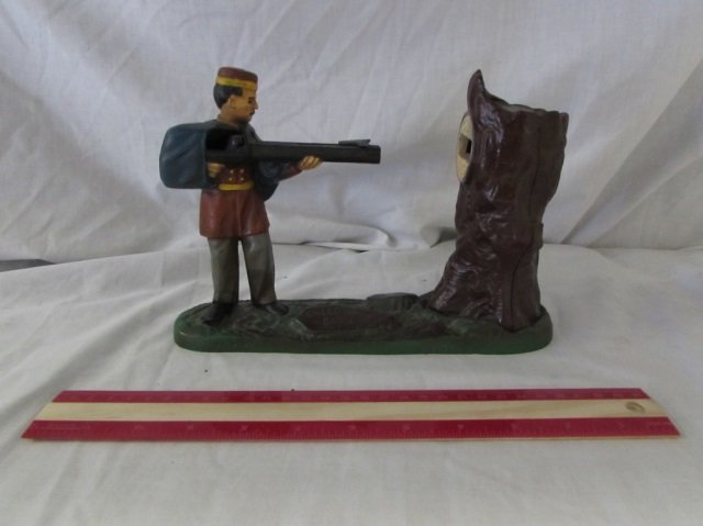 ANTIQUE AMERICAN MECHANICAL COIN BANK: VINTAGE MECHANICAL COIN BANK DEPICTING A MAN HOLDING AND AIMING A GUN AT A TREE, INCLUDES BOOKLET TITLED "SOME FACTS ABOUT ANTIQUE AMERICAN MECHANICAL COIN BANKS," DATED 1957, MARKED "CREED MOOR BANK