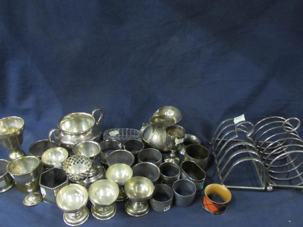 Napkin Rings and Egg Cups: Assortment of 18 napkin rings that are wood, metal, and glass. Nine egg cups that are metal. Also includes a silver plated cream and sugar. and more.