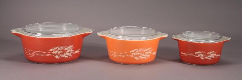 Vintage Pyrex Lidded Bowls (3): Three orange bowls with a wheat design each with a clear glass lid, ranging in size from 8" wide to 11" wide.