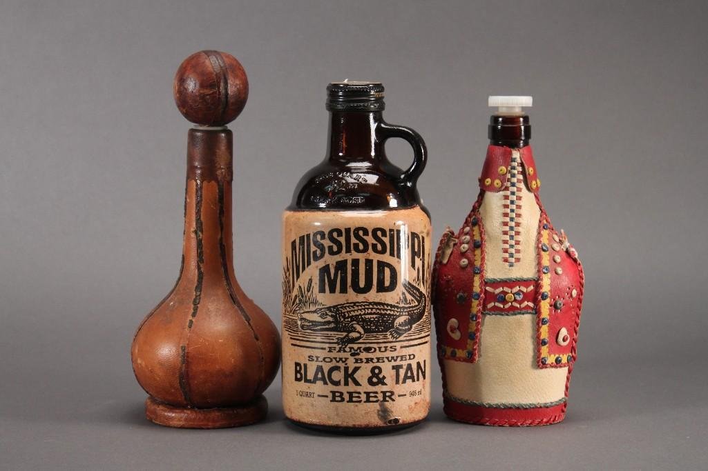 Vintage Leather Wrapped and Beer Bottles (3): Mississippi Mud Black and Tan Beer bottle, 1 qt, 9" tall. Hand made decorative leather covered bottle that measures 8.5' tall, strap is torn. Unique leather covered bottle with round stopper is 9.5" t