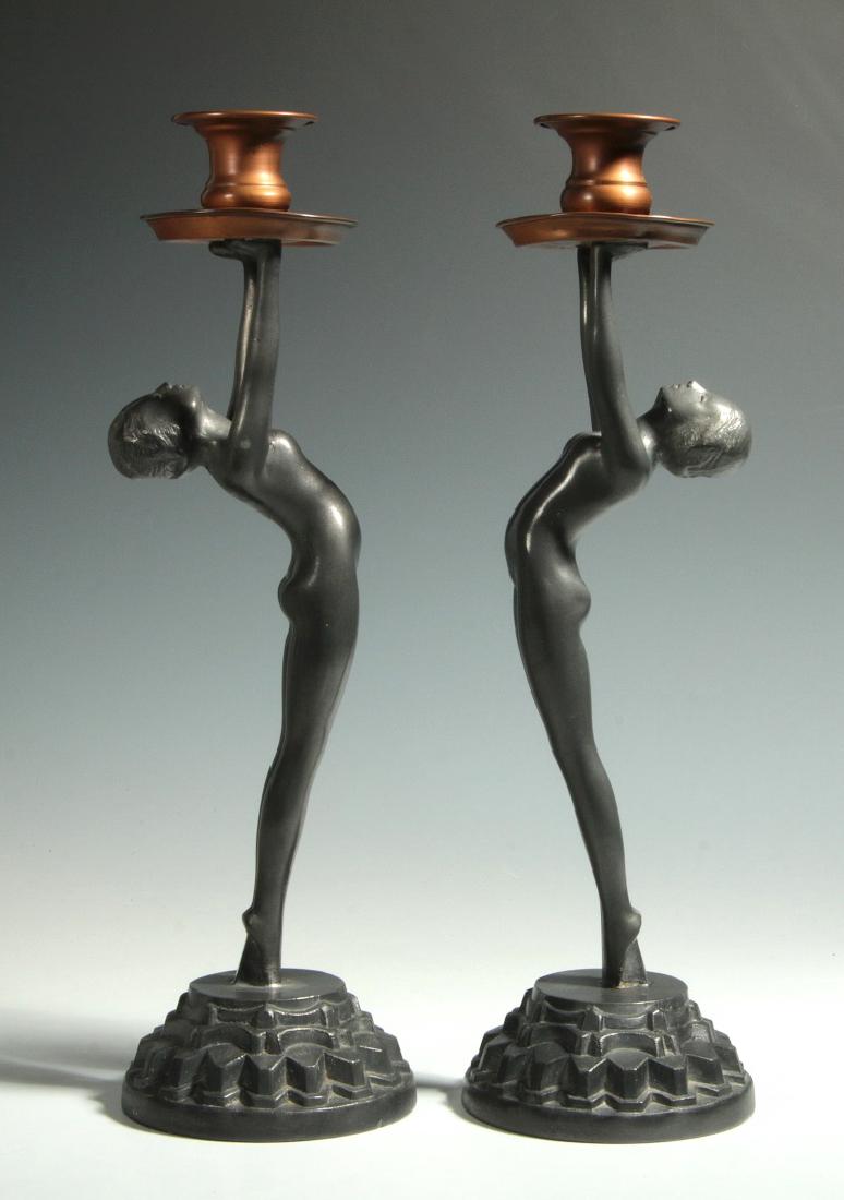 A PAIR OF ART DECO BACK-BENDING NUDE CANDLESTICKS: A pair of circa 1930 standing grey metal nude figures raised on circular stepped cog bases and holding copper candle cups overhead. Unsigned. Each measures 12 inches high. We happily provide seamless 
