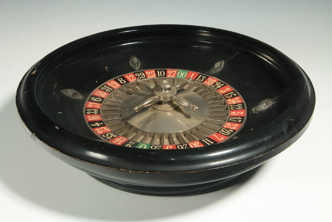 A CIRCA 1900 FRENCH TABLE-TOP ROULETTE WHEEL GAME: An circular ebonised wood frame centered by a nickel-plated wheel with printed paper numeral ring. Stamped 'Made in France' underside of the base. Measures 4 x 14 inches. We happily provide seamless i