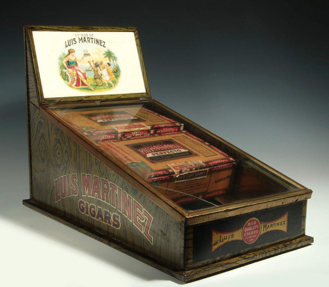 AN EARLY 20TH CENTURY CIGAR ADVERTISING DISPLAY: A circa 1900 tin lithograph counter-top cigar box case with chromolithograph cigar box label top sign framed by a tin frame with wood grain lithography, a slant front case with hinged glass door on wo