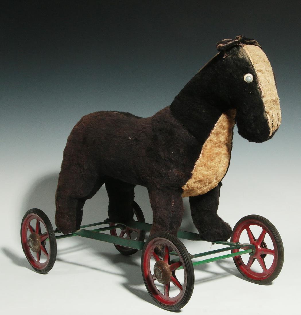 A VINTAGE PLUSH ANIMAL PULL TOY ON WHEELS: An original stuffed toy on iron frame with green paint and original stamped steel spoke wheels in old red paint and with metal hubs. Measures 17.5 x 22 x 9 inches. We happily provide seamless in-house