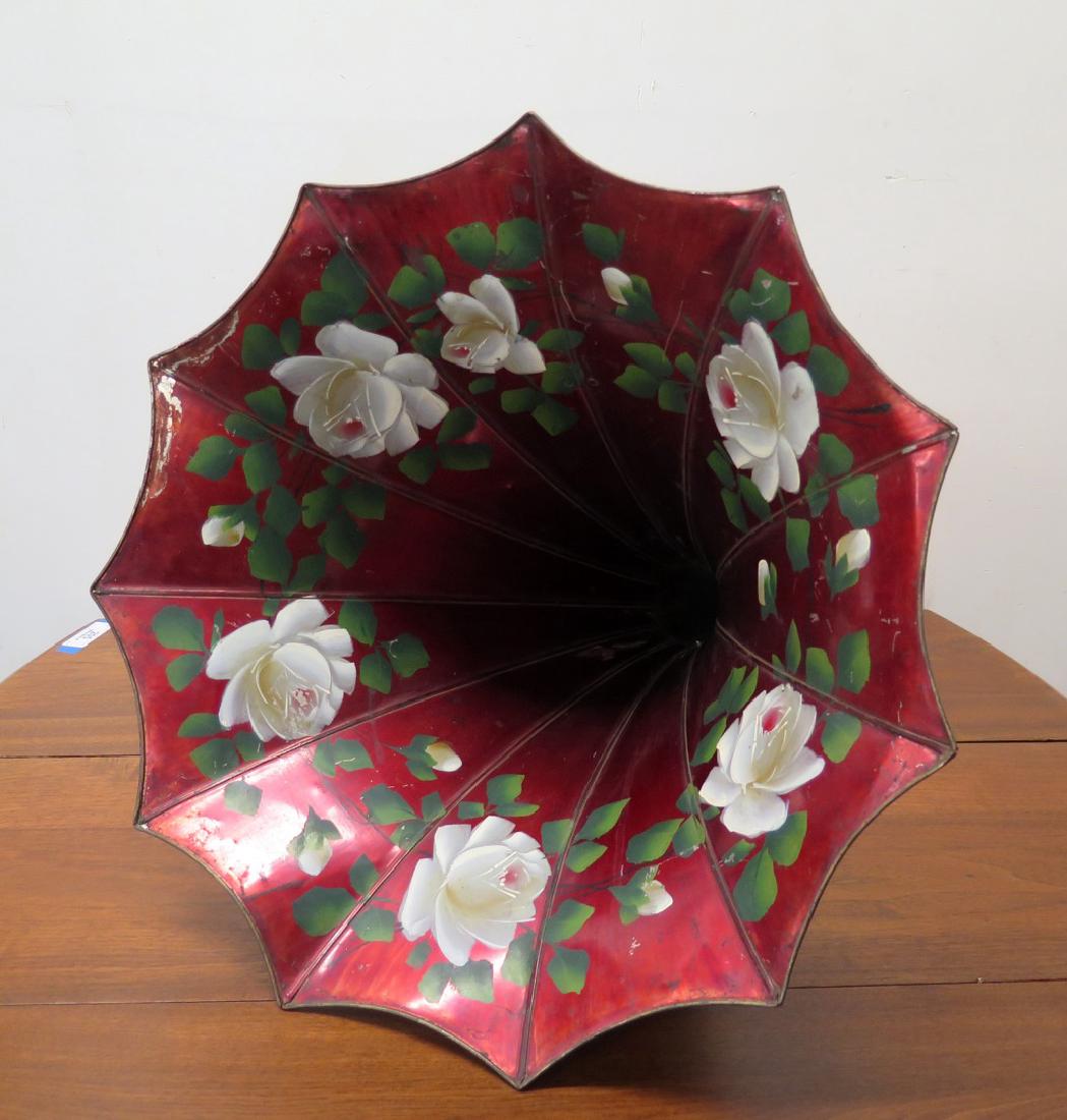 A RED MORNING GLORY PHONOGRAPH HORN WITH FLORALS: Red metal talking machine horn with painted white flowers by Tea Tray Company, early 20th century. Measures 21 x 30 inches.