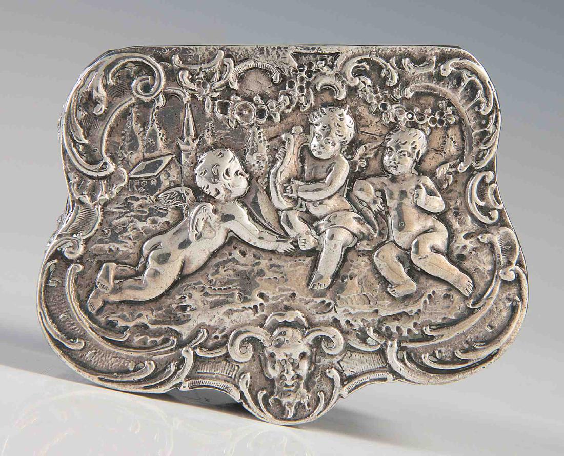 A GOOD LATE 19TH CENTURY .800 SILVER PATCH BOX: A rectangular serpentine box with rounded corners, the hinged lid with cast repoussé scene of three putti encircled by rocaille, the sides of C-scrolls, flowers and foliage, serpentine front incorpor