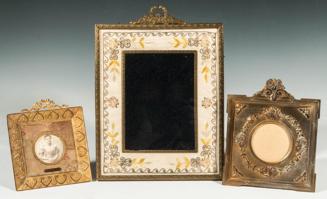 THREE GOOD ANTIQUE FRENCH PICTURE FRAMES: The largest a gilt brass outer frame with laurel leaf and ribbon surmount enclosing an embroidered mat trimmed by a gilt brass leafy trim. Another that is bronze and of square form with floral and scr