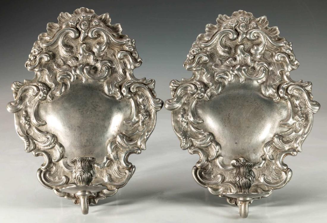 A PAIR CARTOUCHE FORM HEAVILY CHASED PEWTER SCONCES: Each cartouche shaped backplate, shaped outer frame with scrolling vines issuing a single scroll arm terminating in foliate candle cup. Continental touch mark on back side. Measure 11 x 8.5 inches eac